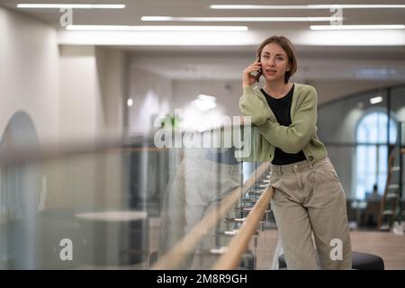 Successful woman talking on phone standing inside business center building calling taxi or courier Stock Photo