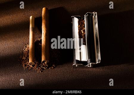 Rolling machine, cigarillos, scattered tobacco on background, cigarette roll with filter, cigarette filters. Stock Photo