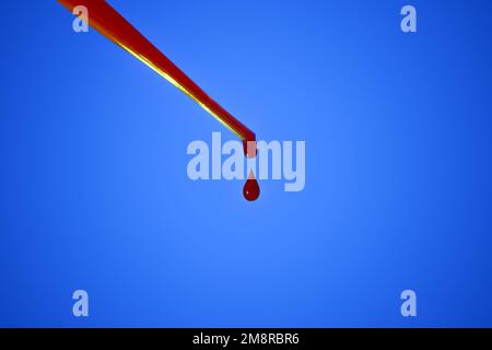 A drop of blood. Pipette. On a blue background. Dripping red liquid. A drop of red. Tests, blood group. Stock Photo