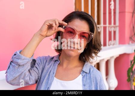 Self assured young lady adjusting sunglasses and looking at camera Stock Photo