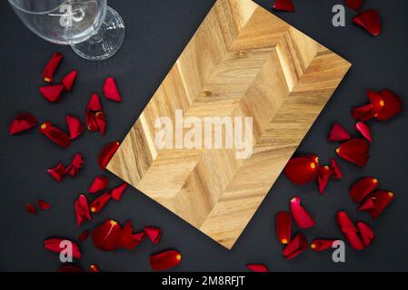 Wooden cutting board for cooking on a dark black background with a glass of wine and red rose petals. View from the top. Stock Photo