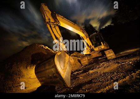 Excavator at night, dramatic lighting and composition, with clouds and stars in the sky in background Stock Photo