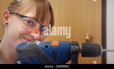 Young woman in protective glasses using drill for home renovation. High quality photo Stock Photo