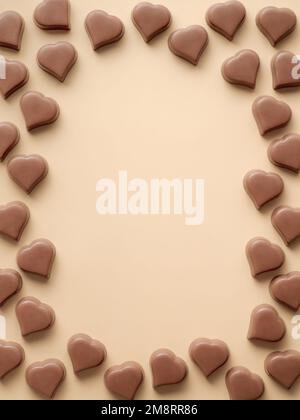 Frame of romantic chocolate confections in heart shapes on pastel yellow background. Canvas with heart chocolate sweets on champagne beige background. Copy space. Valentines day background. Vertical Stock Photo