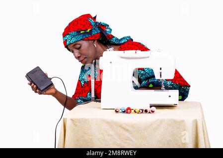 portrait of a beautiful mature woman seamstress sitting in her workshop near her sewing machine. Stock Photo