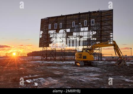 Abandoned outdoor drive in movie theater at sunset with excavator ready for demolition Stock Photo