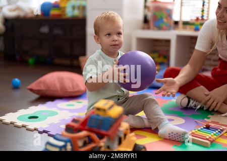 Teacher and toddler playing with ball sitting on floor at kindergarten Stock Photo