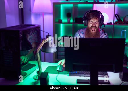 Young redhead man streamer playing video game using computer at gaming room Stock Photo