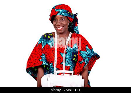 a seamstress in traditional attire standing against white background wearing a sewing machine and looking at the camera smiling. Stock Photo