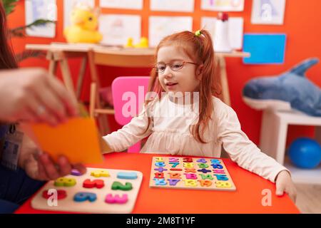 Adorable redhead girl playing with maths puzzle game sitting on table at kindergarten Stock Photo