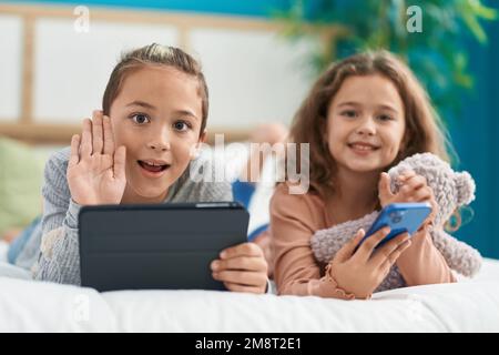 Two kids using smartphone and touchpad lying on bed at bedroom Stock Photo