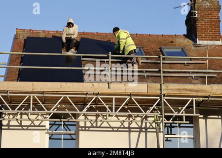 Workmen installing solar panels on roof Stock Photo