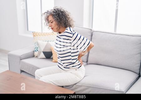 Middle age grey-haired woman suffering for backache sitting on sofa at home Stock Photo