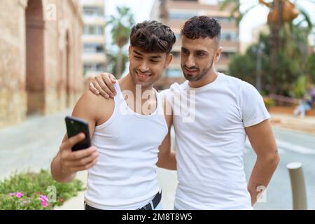 Two hispanic men couple smiling confident using smartphone at street Stock Photo