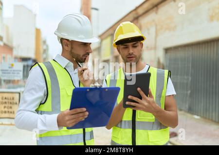 Two hispanic men architects reading document using touchpad at street Stock Photo