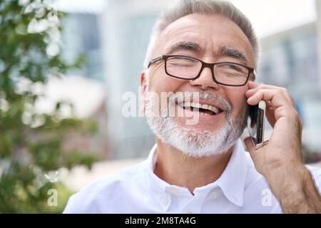 Happy older business man talking on cell phone making call in city outside. Stock Photo
