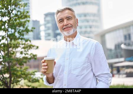 Confident happy mature older business man holding coffee, outdoor portrait. Stock Photo