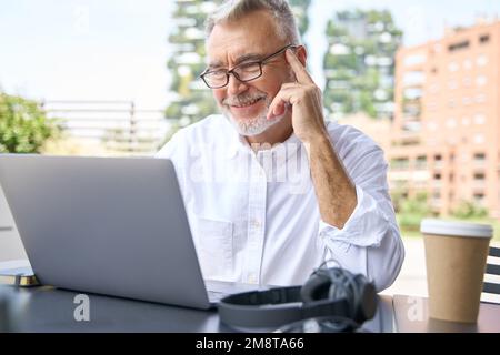 Happy senior business man using laptop computer elearning sitting outside. Stock Photo