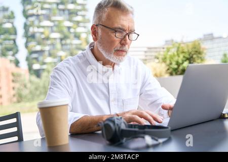 Older senior business man using laptop computer elearning sitting outside. Stock Photo