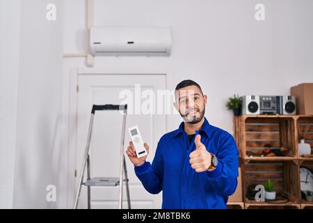 Hispanic repairman working with air conditioner smiling happy and positive, thumb up doing excellent and approval sign Stock Photo