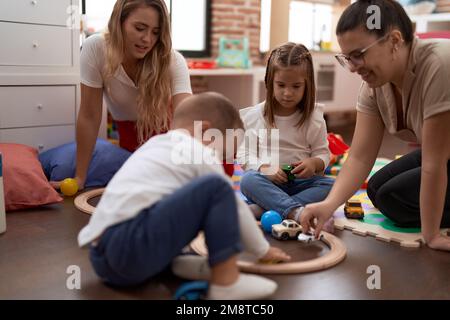 Teachers with boy and girl playing with cars toy sitting on floor at kindergarten Stock Photo