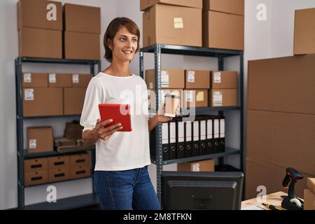 Young beautiful hispanic woman ecommerce business worker using touchpad drinking coffee at office Stock Photo