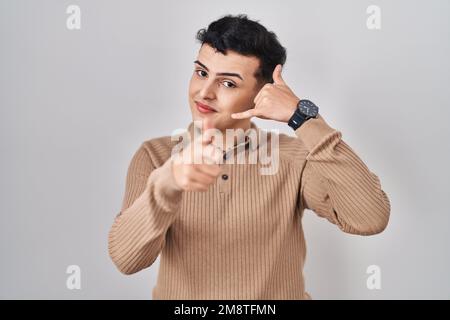 Non binary person standing over isolated background smiling doing talking on the telephone gesture and pointing to you. call me. Stock Photo