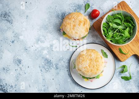 Two homemade sandwiches with ham, cheese and arugula on a concrete table. Stock Photo