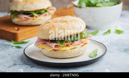 Two homemade sandwiches with ham, cheese and arugula on a concrete table. Stock Photo