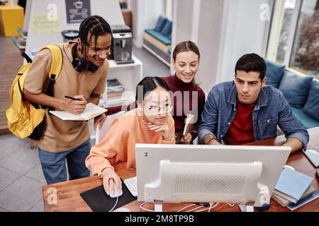 High angle view at diverse group of college students using computer together in library interior Stock Photo