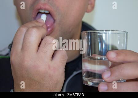 man's hands carrying a pill in his mouth and holding a glass of water in the other hand. Side effects of psychiatric drugs and various medicines. Stock Photo