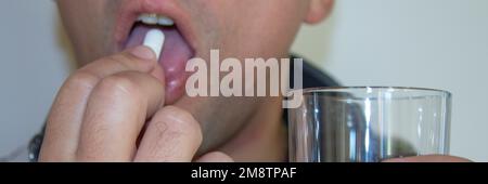 a man's hands carrying a pill in his mouth and holding a glass of water in the other hand. Side effects of psychiatric drugs and various medicines. Stock Photo