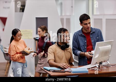 Portrait of students in college library focus on two young men using computer in foreground, copy space Stock Photo