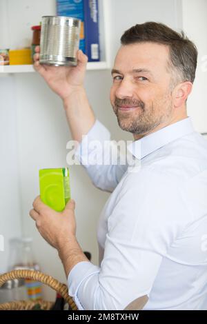 man putting away shopping in the kitchen cupboard Stock Photo