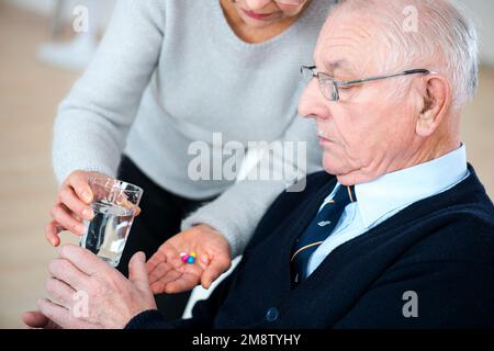 caring senior wife giving pills to his ill husband Stock Photo