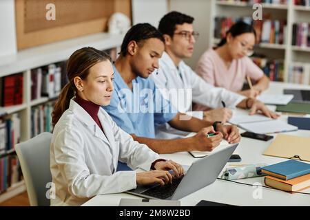 Diverse group of young med students sitting in row at table during lecture or seminar Stock Photo