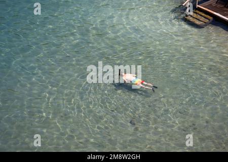 Aerial view to sea and man in scuba mask swimming in transparent water. Snorkeling and diving on shallow, beach vacation Stock Photo