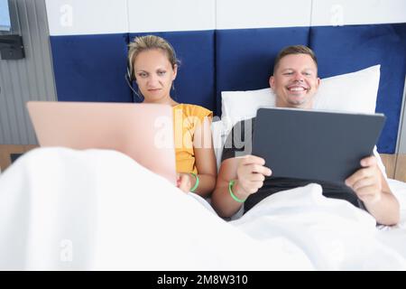 Couple of freelancers lying in bed with laptops and working. Stock Photo