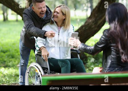 Deceased woman in wheelchair with her friends having fun while walking in park. Stock Photo