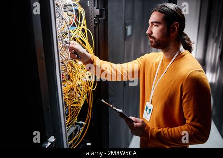 Side view portrait of bearded technician working with server network and connecting cables Stock Photo