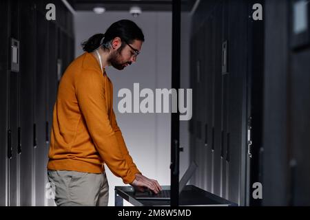Minimal side view portrait of bearded network engineer using laptop in server room Stock Photo
