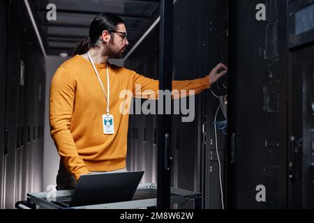 Waist up portrait of bearded network engineer using laptop while working in server room Stock Photo