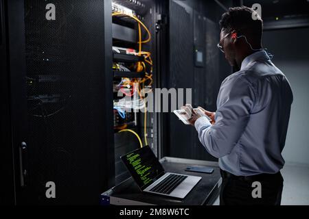 Side view portrait of network engineer using laptop while setting up servers in data center Stock Photo