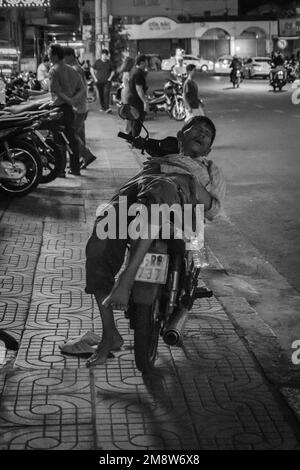 black and white man sleeping on his moped motorcycle in the street by night in Ho Chi Minh Vietnam Stock Photo