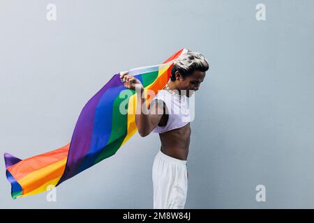Side view of a young stylish man in stylish clothes walking with rainbow LGBT flag Stock Photo