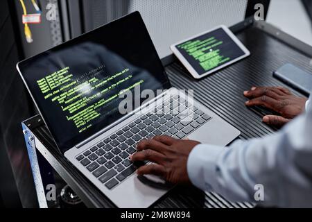 High angle close up of network engineer or hacker using laptop with green code lines in server room, copy space Stock Photo