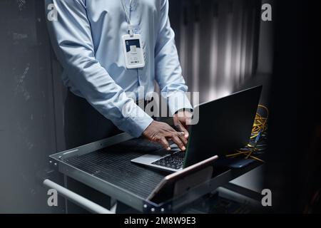 Close up of black man typing at laptop keyboard while setting up network in server room, copy space Stock Photo