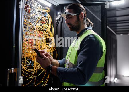 Side view portrait of bearded network technician repairing servers in data center, copy space Stock Photo