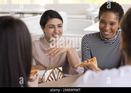 Happy Indian and African female friends eating pizza in cafe Stock Photo
