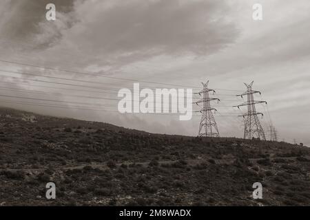 Pylons overhead power lines on foggy mountain and cloudy winter sky. Black and white tint. Stock Photo